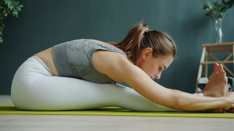 A woman in activewear stretching on a yoga mat indoors, focusing on wellness and fitness