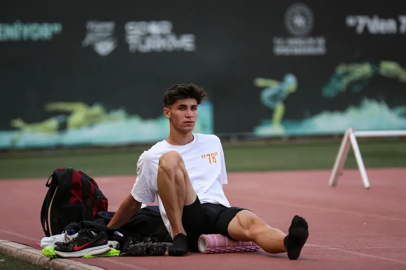 Athlete in sportswear using a foam roller on a track, preparing for training