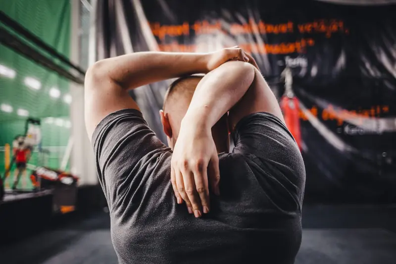 Man stretching arms in a gym, viewed from behind, focusing on fitness and flexibility