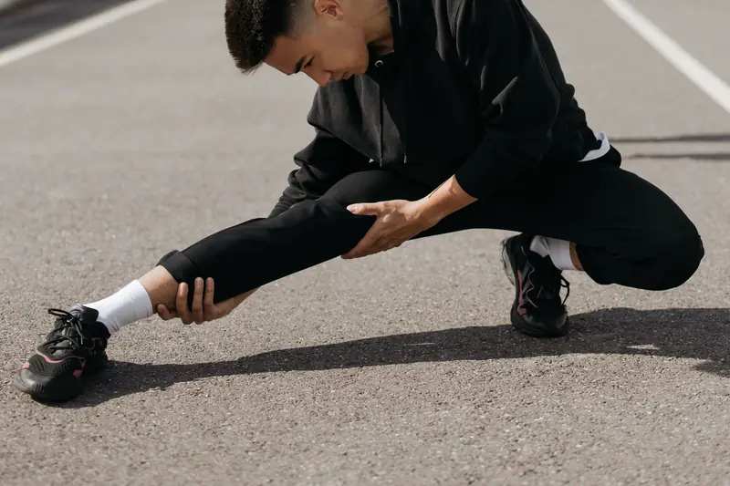 A young man performs stretching exercises on a city street, focusing on flexibility and fitness
