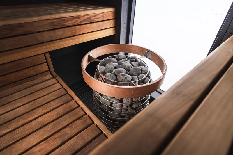 A cozy modern sauna with a wooden interior and a central heater with stones, ready for relaxation