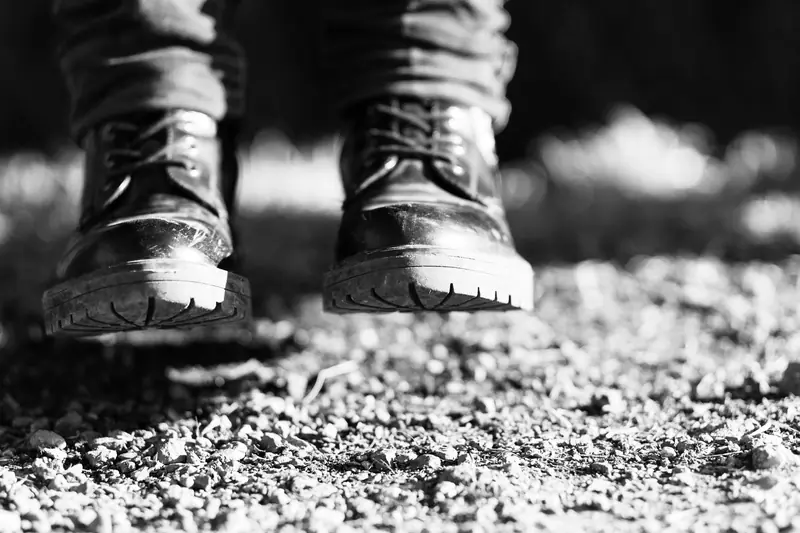 Close-up black and white shot of boots on a gravel surface, emphasizing texture