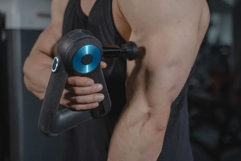 Close-up of a man using a massage gun for muscle relaxation on his arm