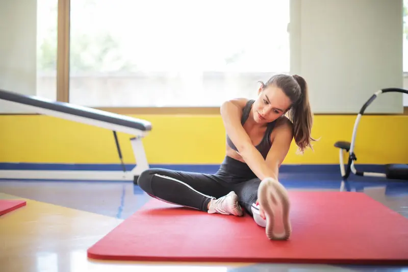 Female athlete stretching on a red yoga mat indoors, emphasizing flexibility and fitness