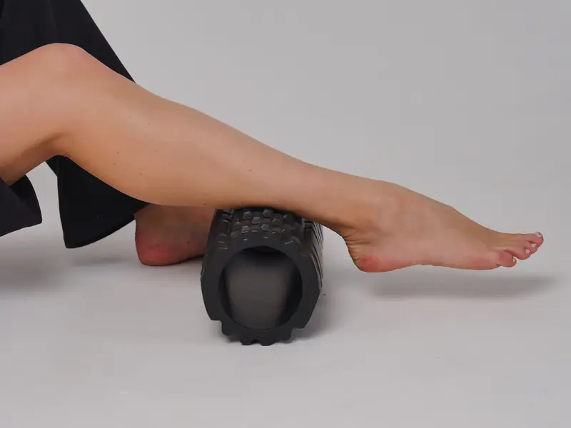 Close-up of a leg using a foam roller for stretching and muscle relief in a studio setting